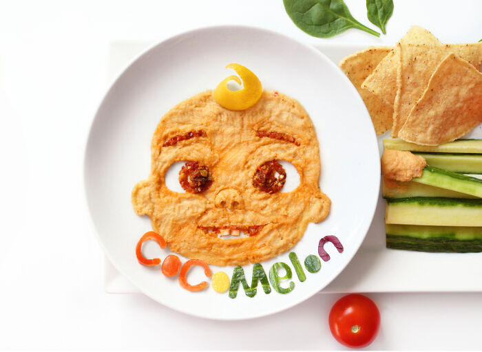 Playful food art design inspired by cartoons, using fresh ingredients to create a baby face on a plate with vegetables and chips.