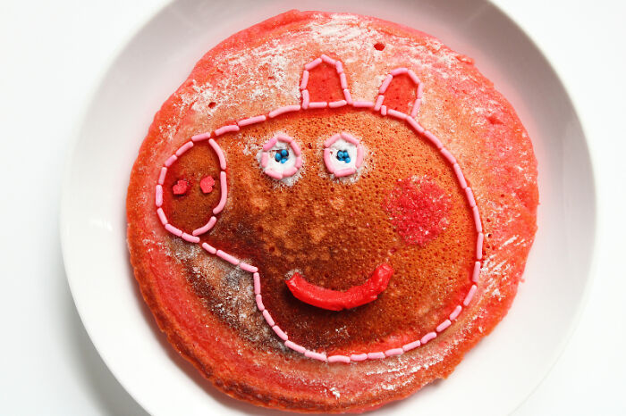 Cartoon-inspired food art using fresh ingredients on a pancake designed like an animated character face.