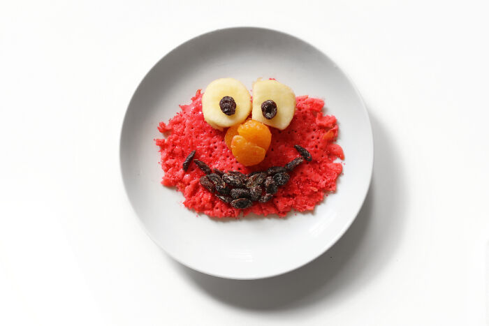 Playful food art design using fresh ingredients to create a cartoon character face on a white plate.