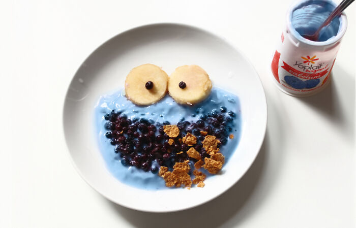 Playful food art design using fresh ingredients inspired by cartoons, featuring blueberries and yogurt on a plate.