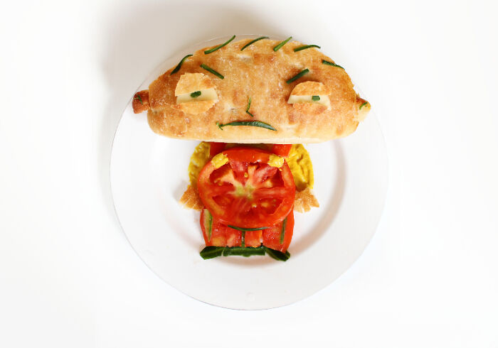 Playful food art design using fresh ingredients, resembling a cartoon character with a sandwich head on a white plate.