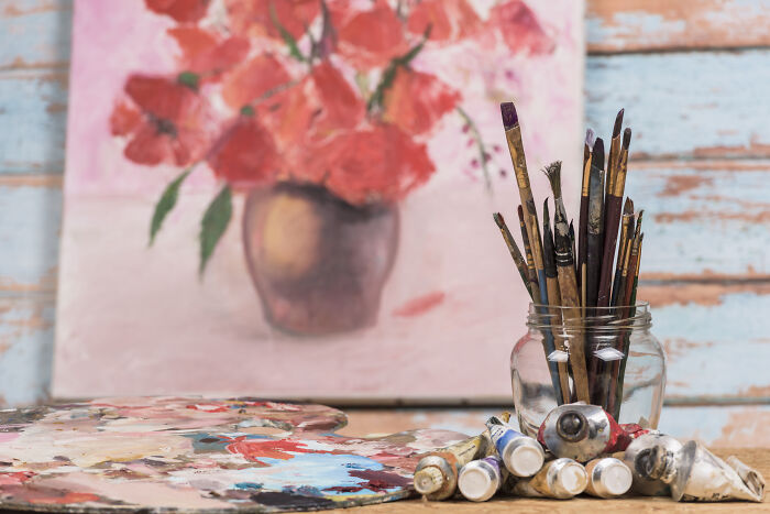 Art supplies including paint tubes, brushes, and a canvas with red flowers.