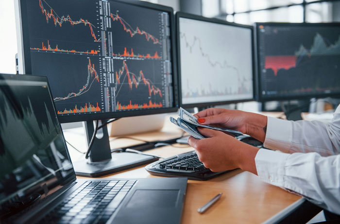 Person holding cash in front of monitors showing stock graphs, relating to UnitedHealth's $63 billion value loss.