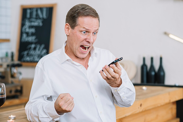 Man in a white shirt expressing excitement during a phone call in a modern cafe setting.