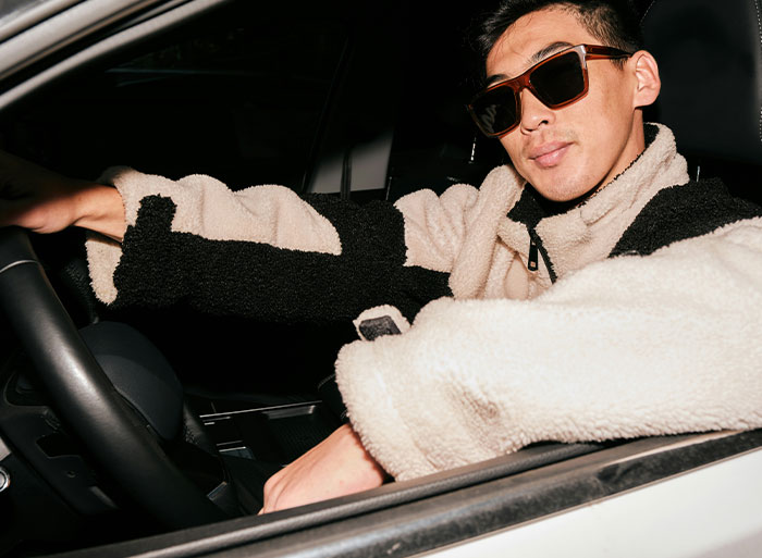 Man in sunglasses and a cozy jacket confidently sitting in a car, embodying self-assuredness after a clever act of revenge.