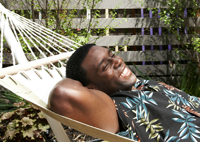 Man relaxing in a hammock, smiling under the sun at a resort, feeling satisfied after achieving petty revenge.