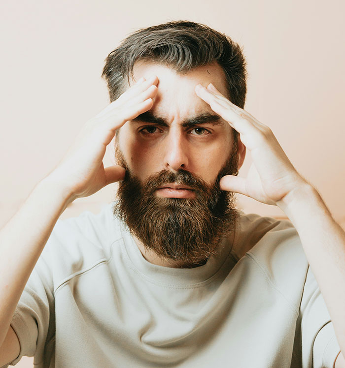 Bearded man looking stressed, wearing a light sweatshirt, representing long work shifts with minimal rewards.