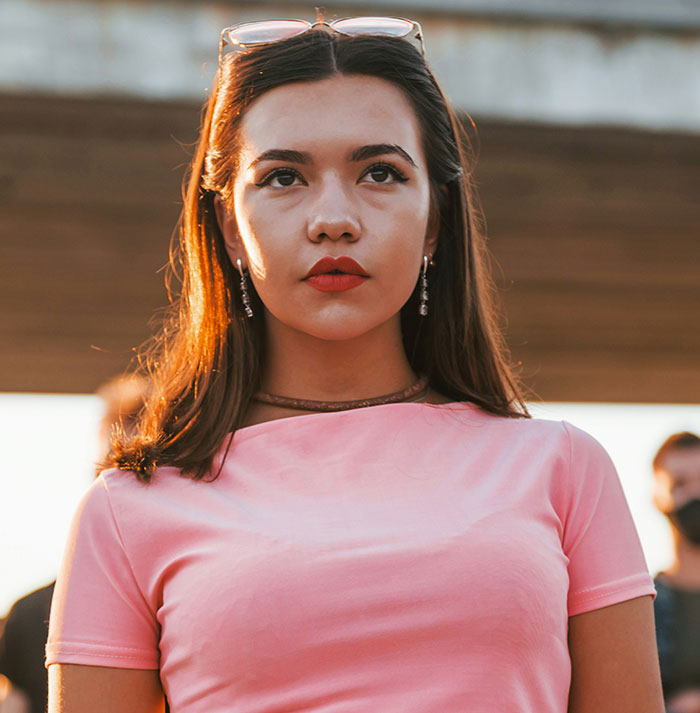 Teen in a pink shirt looking contemplative, with her hair down, outside on a sunny day.