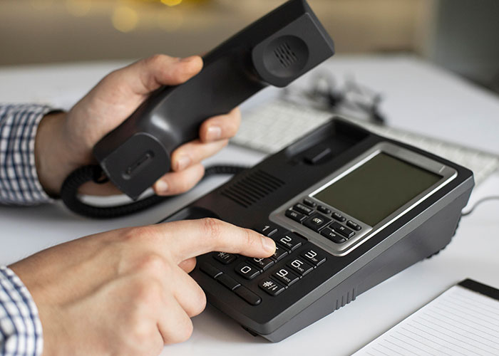 Older person teaching grandparent how to use a modern office phone, pressing buttons, and holding the receiver.