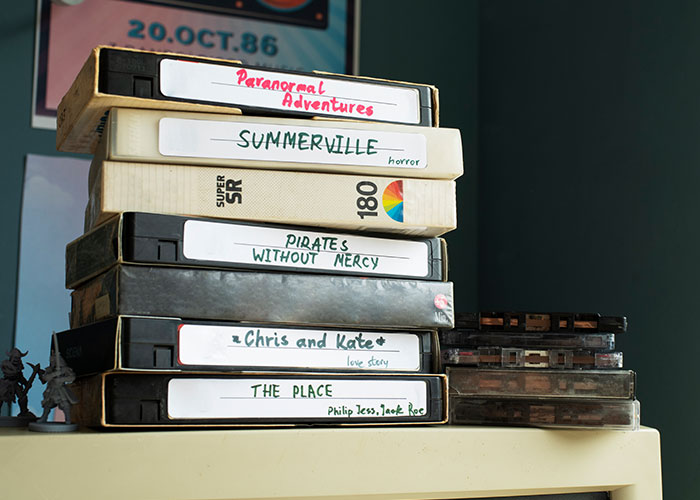 Stack of labeled VHS tapes, including titles like "Paranormal Adventures" and "Pirates Without Mercy," evoke nostalgia.