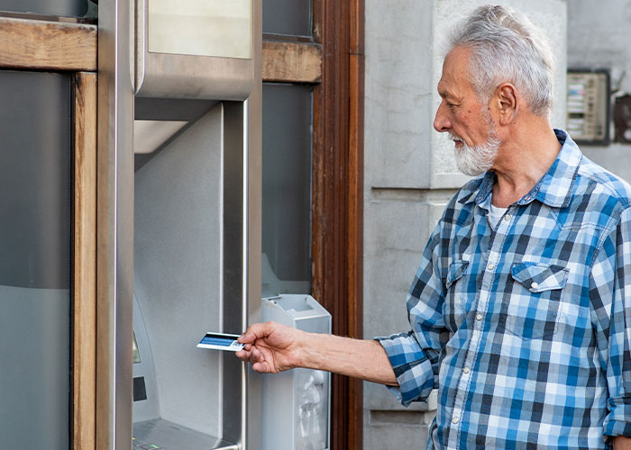 Older person using an ATM, wearing a blue plaid shirt, demonstrating technology skills.