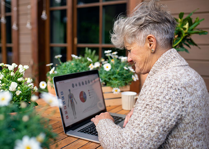 Older person enjoying teaching technology to grandparent, using laptop in a garden setting with flowers.