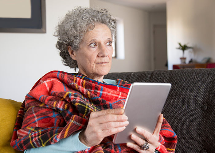 Older person using a tablet, wrapped in a red blanket, reflecting on teaching moments with grandparents.