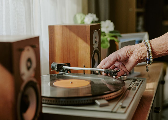 Older person adjusting a record player, showing a classic music setup with wooden speakers.