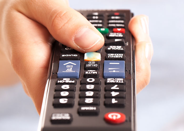 A hand holding a TV remote control, illustrating older people teaching grandparents technology basics.