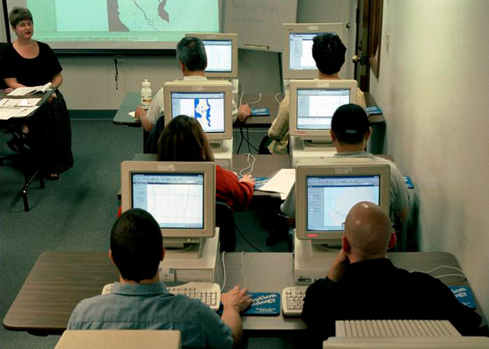 Older people in a computer class sharing knowledge with grandparents; instructor at front.