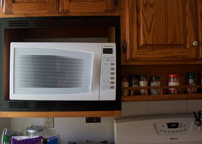 A kitchen scene with a microwave oven surrounded by wooden cabinets and a spice rack, connected to older people teaching moments.