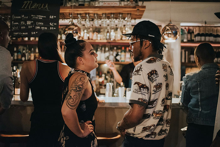 A man and woman engage in conversation at a bar with dim lighting and a busy background.