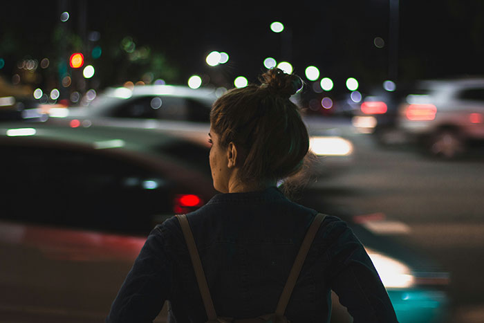 Woman standing alone on a busy city street at night, lost in thought.