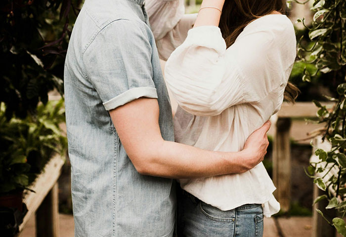 A man in a denim shirt embraces a woman in a garden setting, illustrating creepy things done unknowingly.