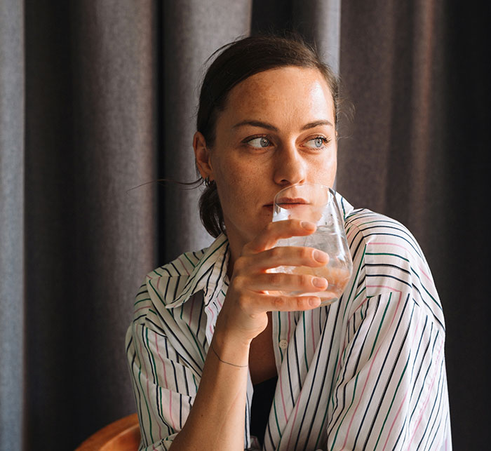 Woman sitting with a drink, wearing a striped shirt, looking thoughtful; exploring social interactions.