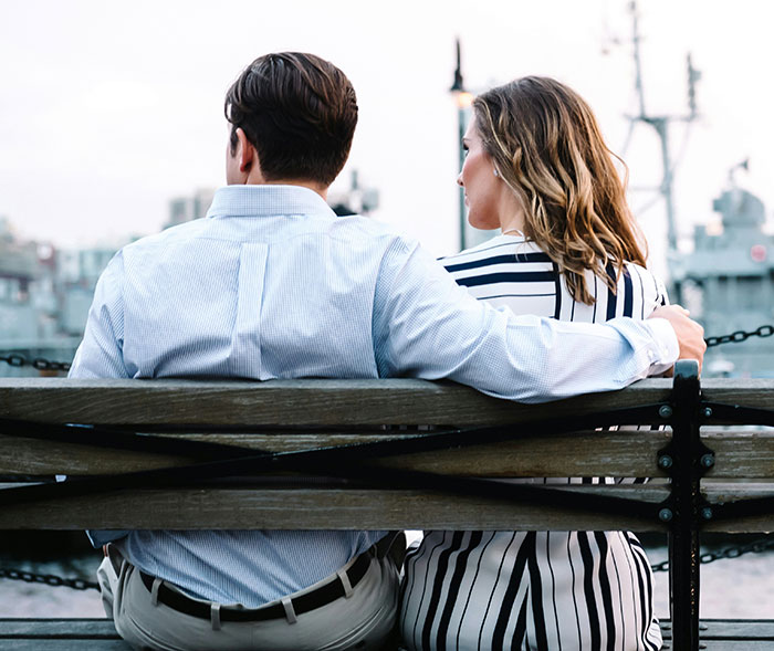 Man and woman sitting together on a bench by the waterfront, highlighting social interactions with subtle intimacy.