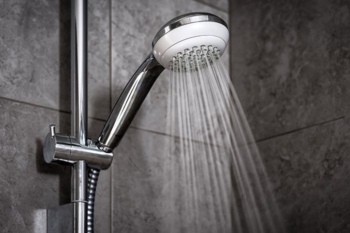 Shower head with water flowing against a tiled wall, highlighting daily routines like washing rice.