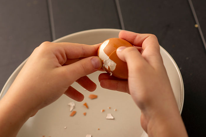 Hands peeling a boiled egg over a plate, focusing on kitchen tasks that might be done wrong, similar to how one washes rice.