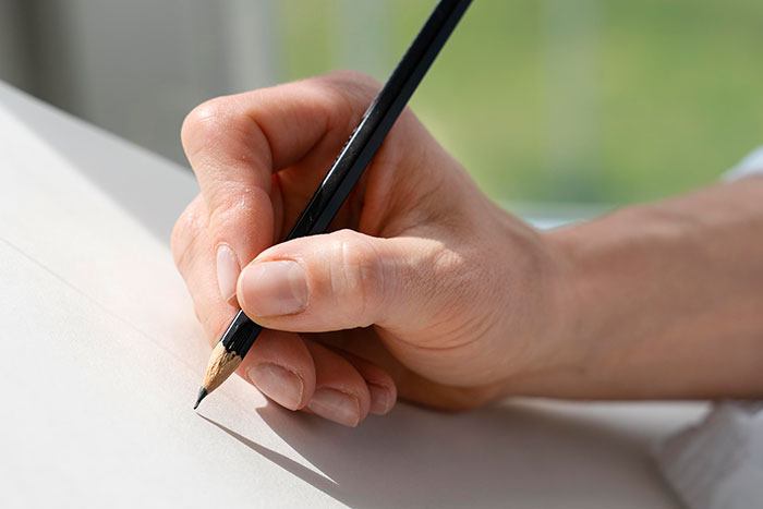 A hand holding a pencil, poised to write on blank paper, highlighting common mistakes in daily tasks like washing rice.