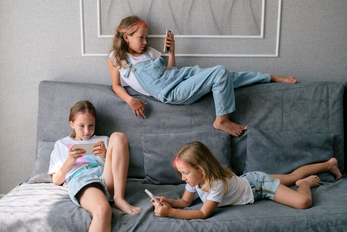 Children using smartphones on a couch, depicting a possible sign of horrible parenting.