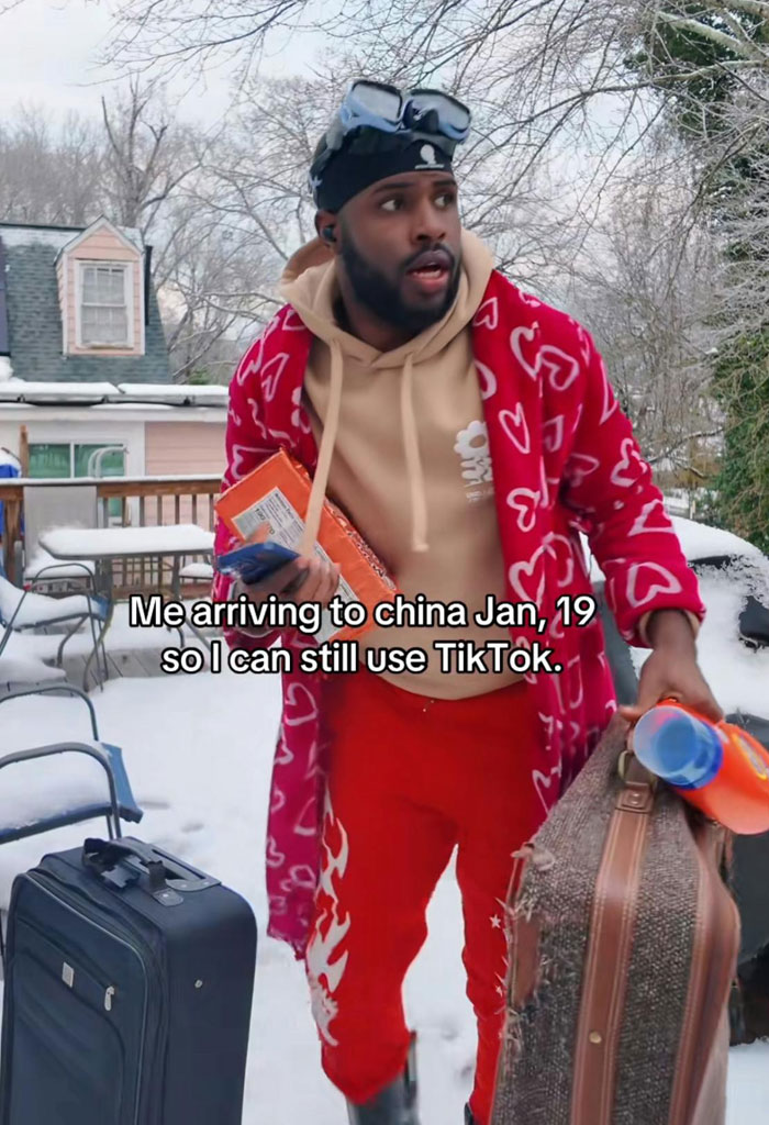 Man in winter attire humorously packing to avoid TikTok ban in America, holding suitcase and snacks outdoors.