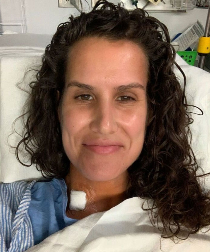 Woman in hospital bed after TikTok advice saves her, smiling with bandage on neck.