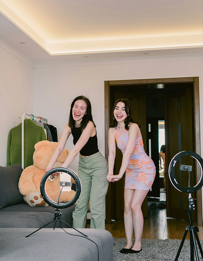 Two women smiling in a living room with ring lights, creating content related to TikTok ban discussions.