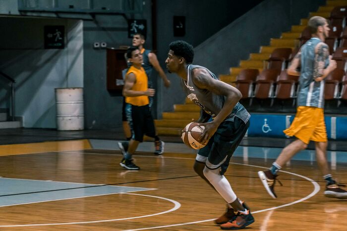 Basketball players in a gym during a game, focusing on a player dribbling.