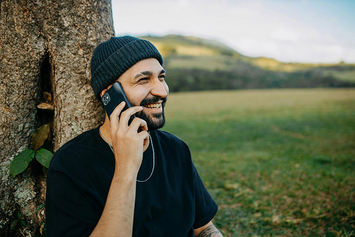 Man smiling and talking on phone outdoors, planning petty revenge on towing company.