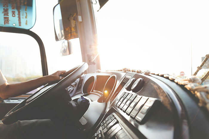 Driver in a tow truck cab, steering with sunlight streaming in, related to towing company dispute.