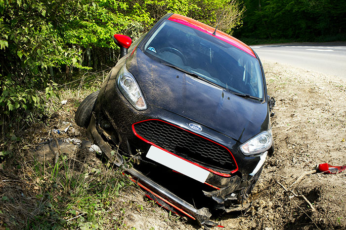 A black car stuck in a ditch with damaged front, surrounded by trees, related to a towing company issue.