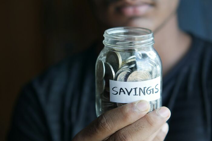 Person holding jar labeled "savings" filled with coins.