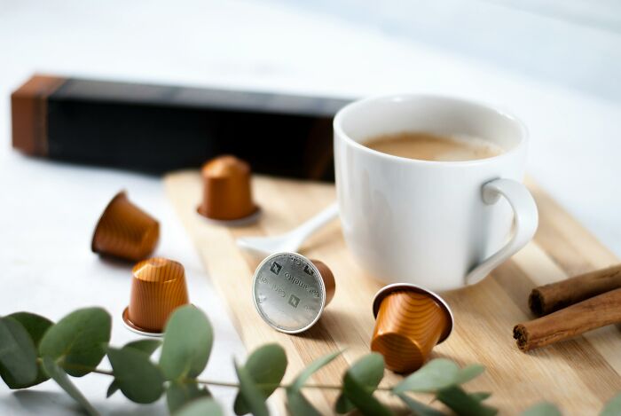 Coffee pods and a white cup on a wooden tray, featuring cinnamon sticks and eucalyptus leaves, symbolizing potentially toxic things.