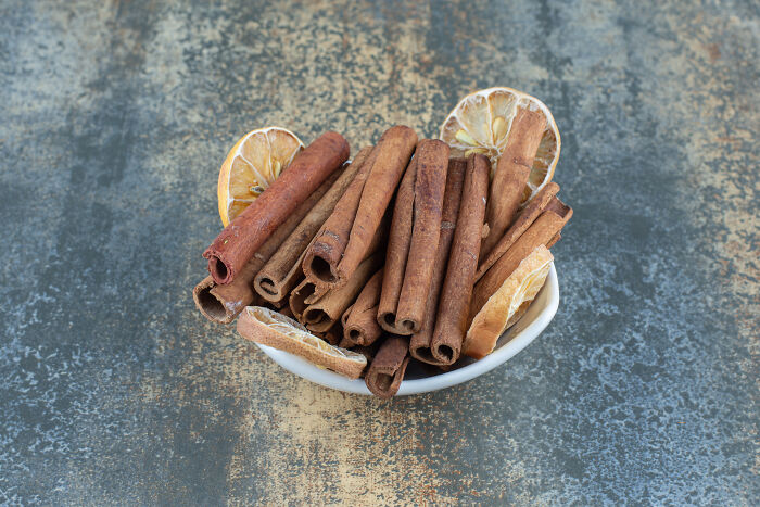 A white bowl filled with cinnamon sticks and dried lemon slices on a textured surface, highlighting toxic things for the body.