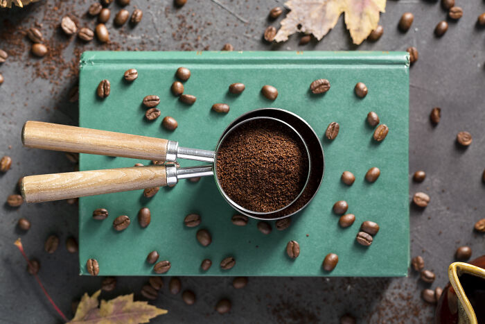 Ground coffee in a metal scoop on a green book with scattered coffee beans, related to toxic things for the body.