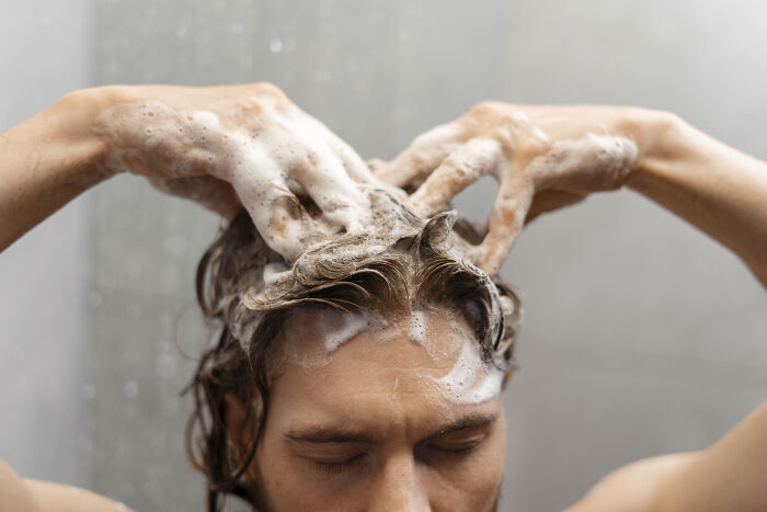 Person washing hair with shampoo, illustrating toxic things for body care.