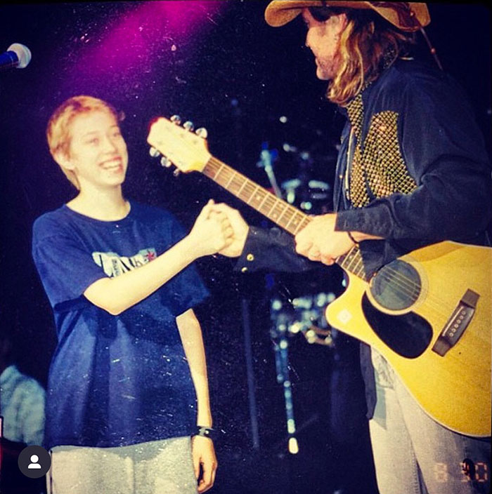 Two people on stage, one with a guitar and cowboy hat, shaking hands under stage lights.