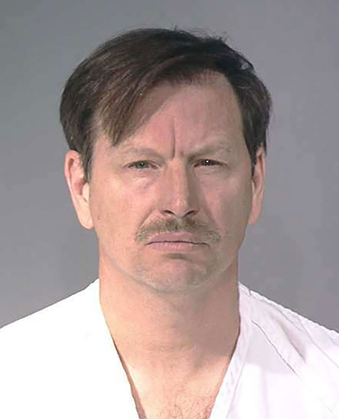 A man in a white shirt, representing a true crime case with plot twists, stares neutrally at the camera.