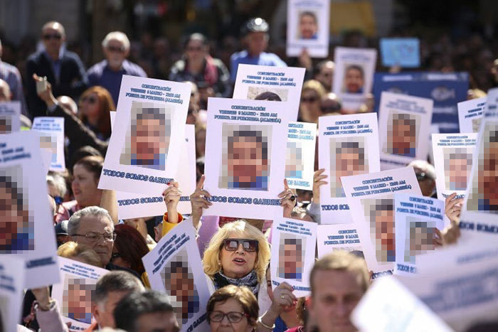 Protesters holding signs related to true crime cases plot twists during a demonstration.