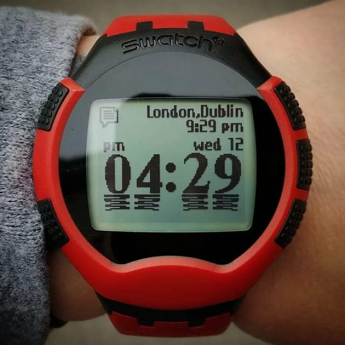 Digital wristwatch with red and black design, displaying time and world cities, an innovative historical invention.