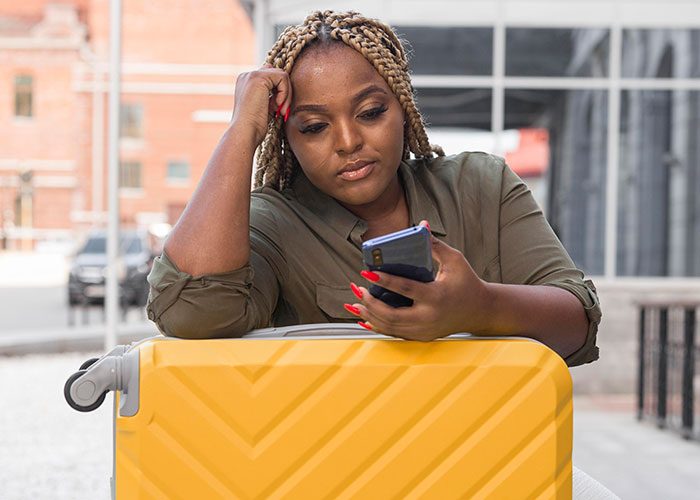 Woman sitting with a suitcase, looking at her phone, reflecting on friendship during a trip.