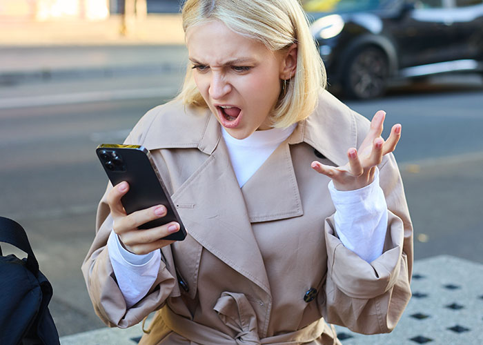 Woman looks surprised at her phone, expressing emotion during a solo trip endeavor.