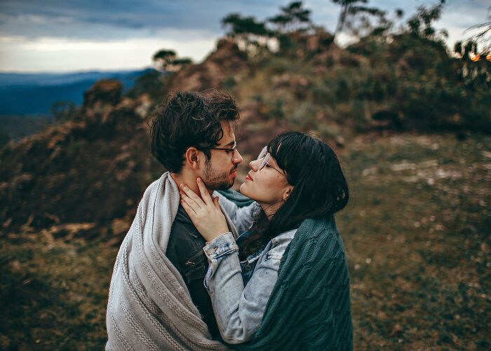 A couple wrapped in blankets sharing an intimate moment outdoors, reflecting an unreasonable friend relationship dynamic.