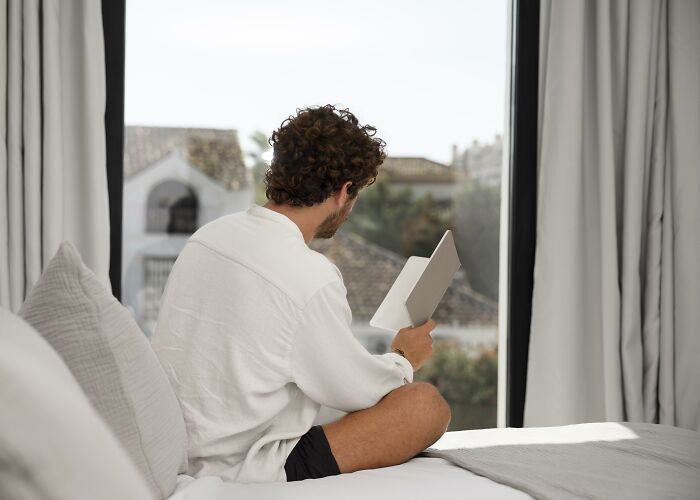 Person with tablet by window, reflecting on an unreasonable friend relationship.